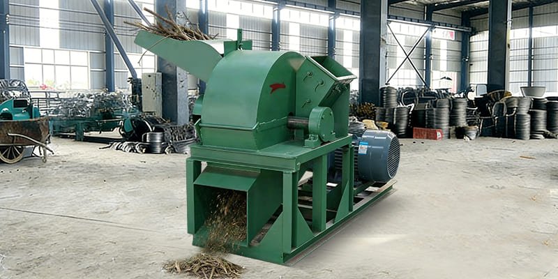 A hammer mill grinding wood branches into fine powder.