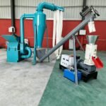 Complete wood pellet production line equipment in factory workshop, including hammer mill, cyclone dust collector, screw conveyor and wood pellet machine, ready for delivery