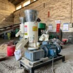 Flat die wood pellet mill machine in workshop, equipped with large feed hopper, electric motor and stable base frame for biomass pellet production